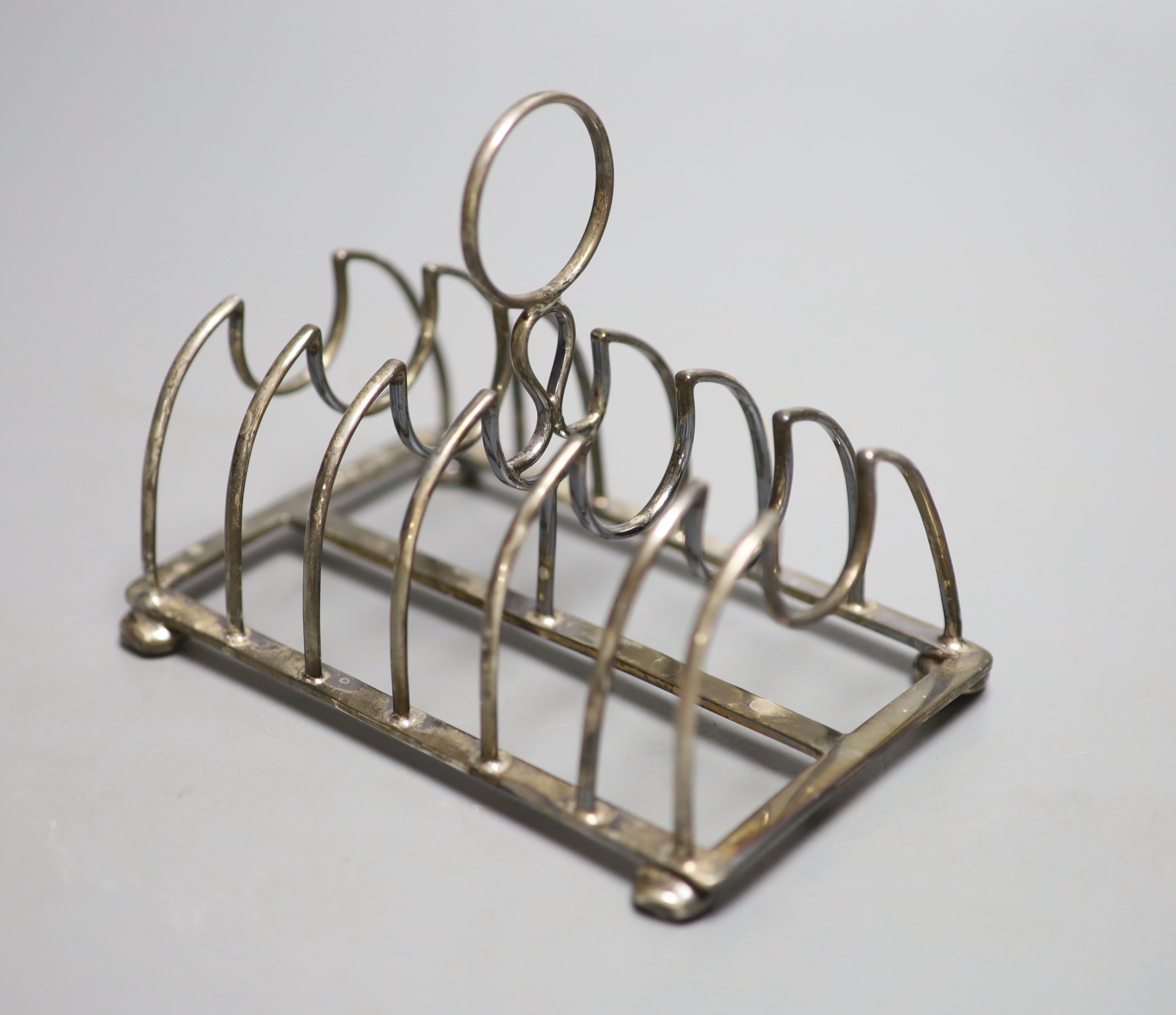 A late Victorian silver seven bar toastrack, on bun feet, Nathan & Hayes, Chester, 1900, length 13.6cm,